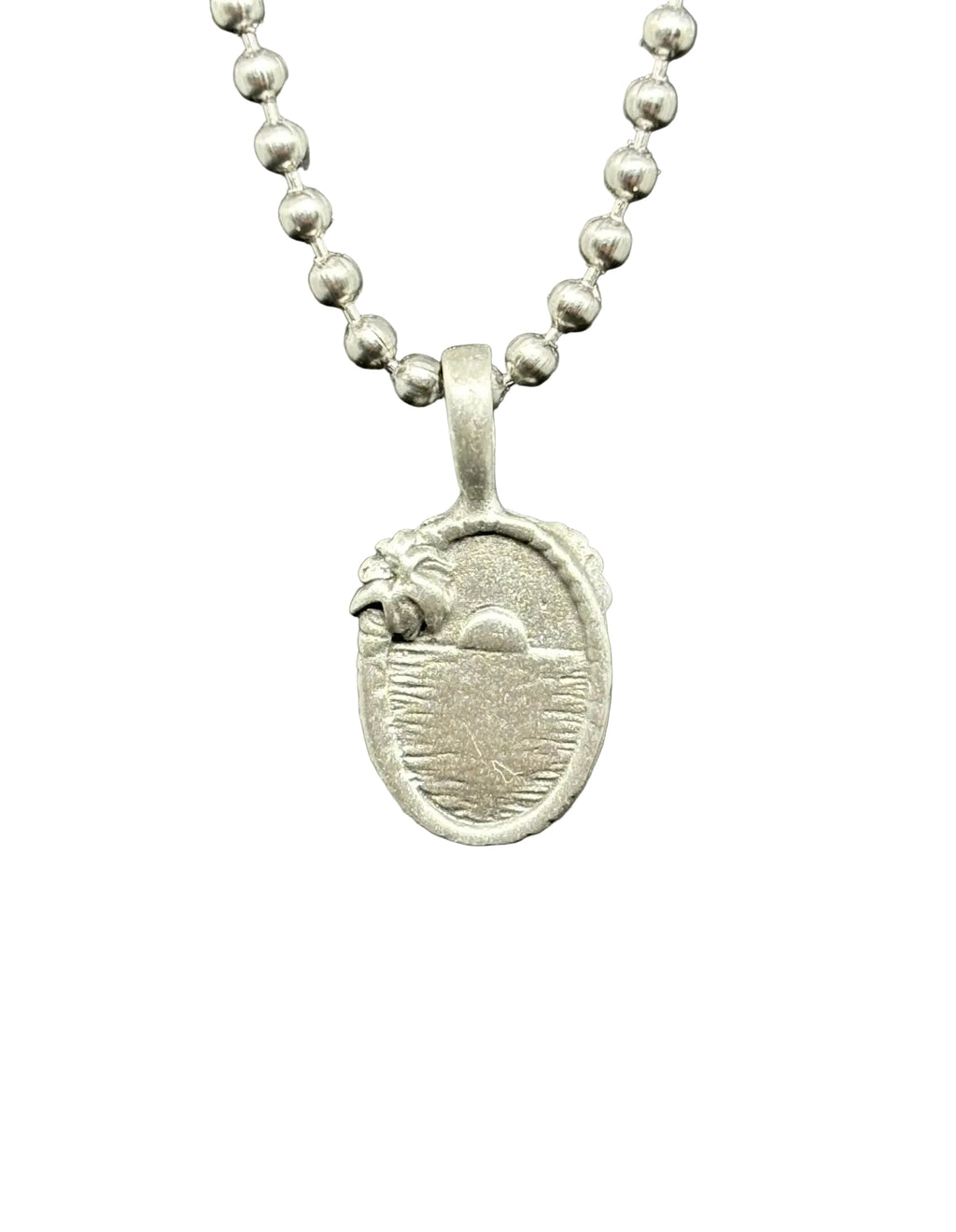 A silver oval pendant necklace featuring a detailed relief design of a bird and sun over water, suspended from a silver ball chain against a dark gray textured background.
