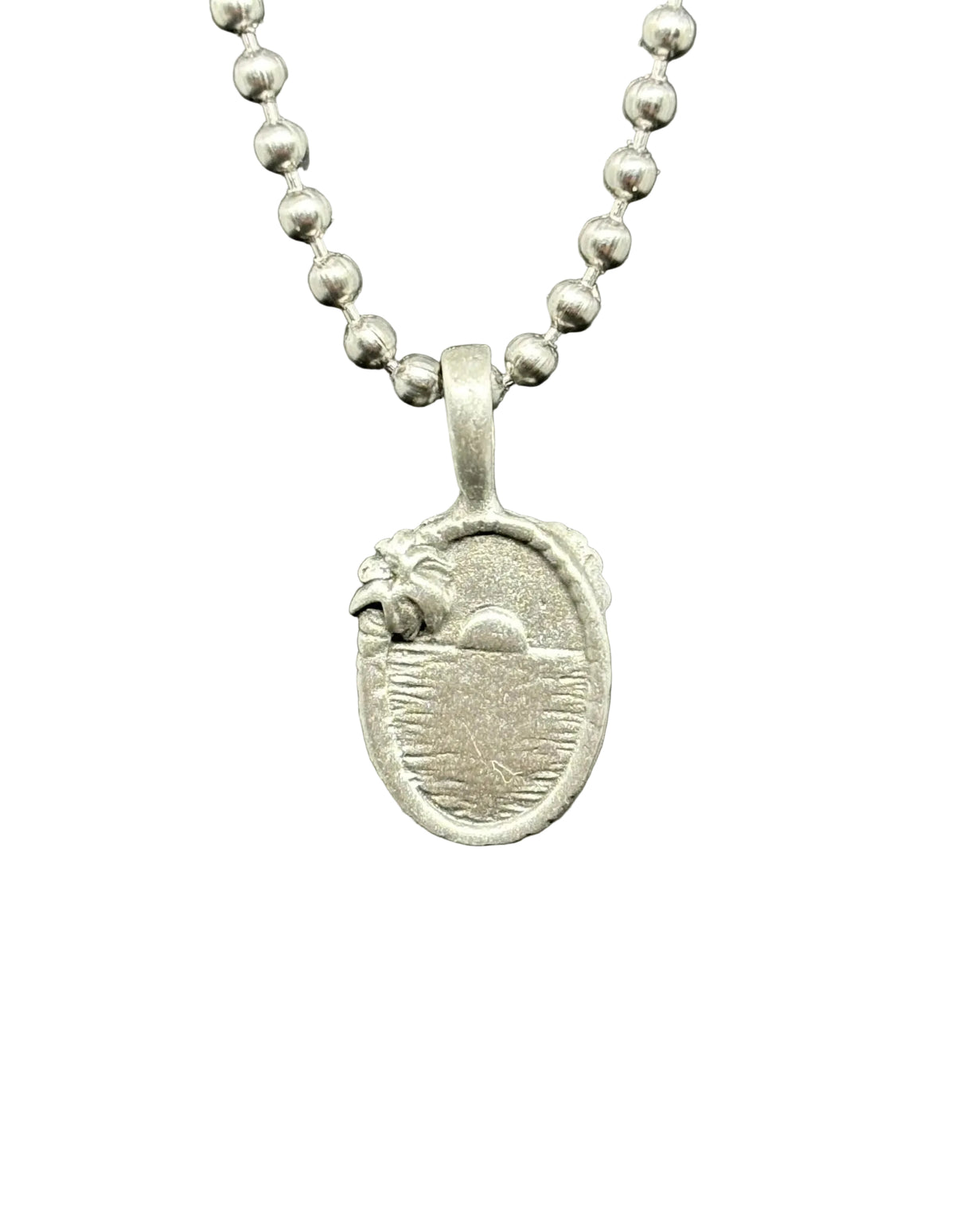 A silver oval pendant necklace featuring a detailed relief design of a bird and sun over water, suspended from a silver ball chain against a dark gray textured background.